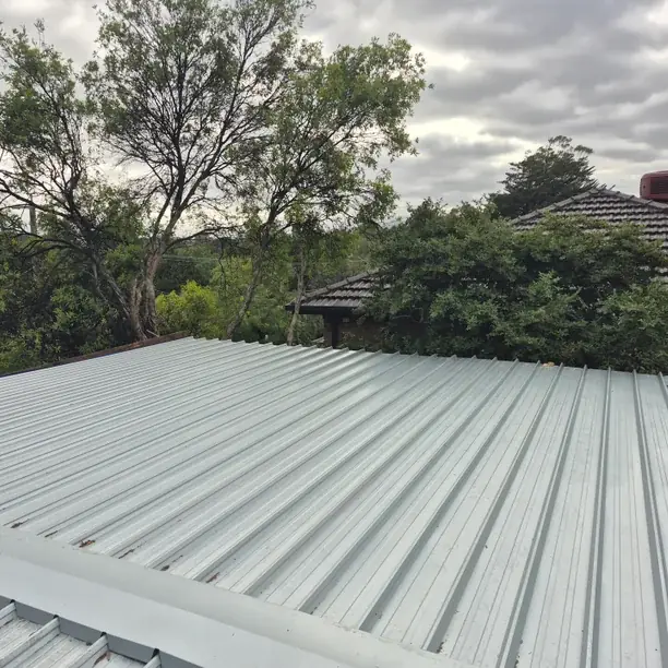 Looking along a finished light-coloured corrugated metal roof to the gutter line, with gum trees behind