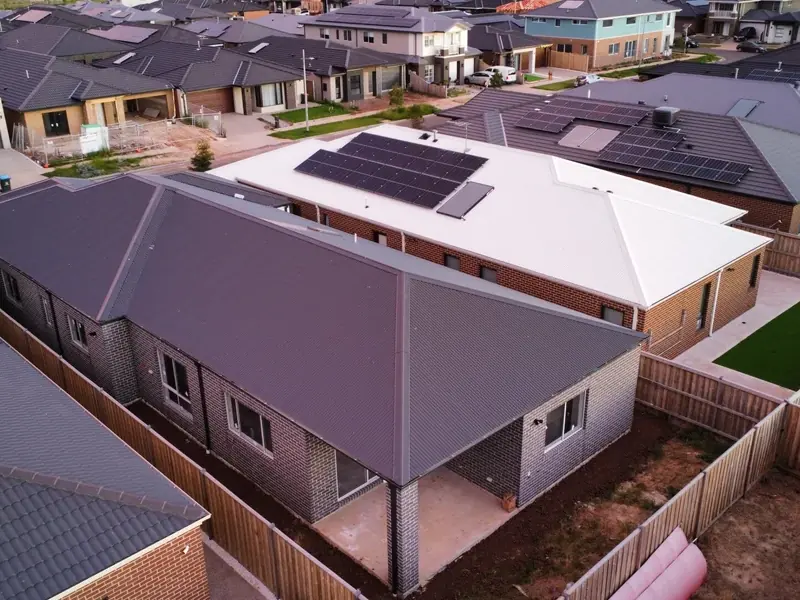 Drone view of a new single-storey home with a dark hip metal roof among tiled houses in a new estate