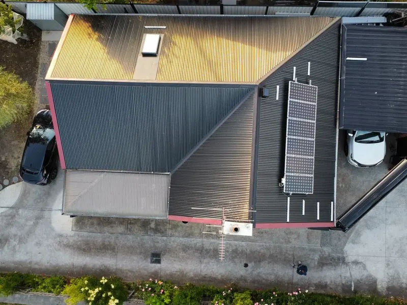 Top-down drone view of a house re-roofed in dark metal, with a solar panel array, a skylight and a lighter metal section at the back