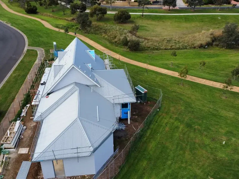 Drone view of a new home with a multi-hip light grey metal roof, backing onto parkland