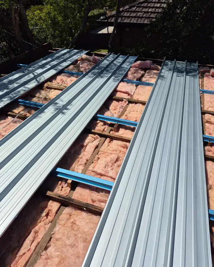 New metal roof sheets going down over battens, with insulation batts and sarking underneath