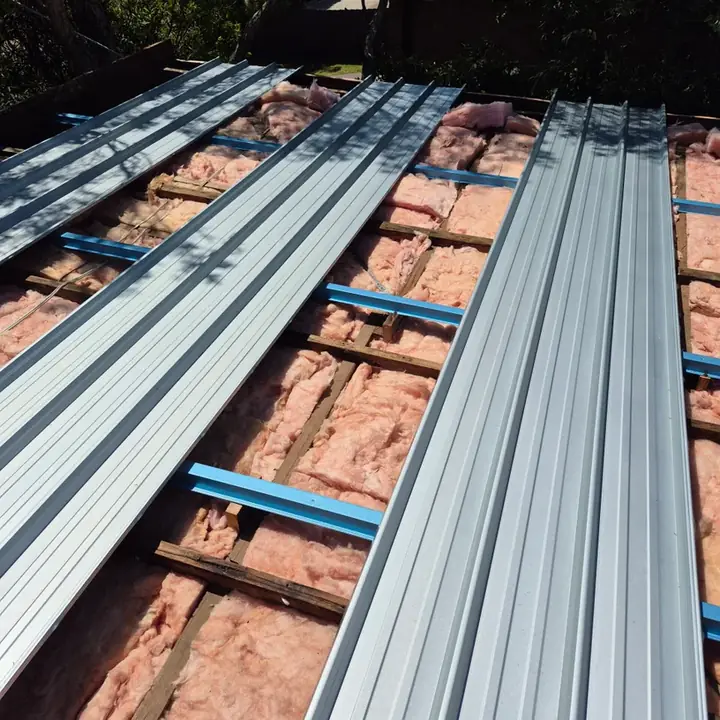 New metal roof sheets going down over battens, with insulation batts and sarking underneath