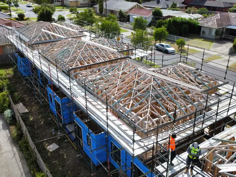 Drone view of a row of new units in scaffolding, the roof trusses up and a crew on the frame